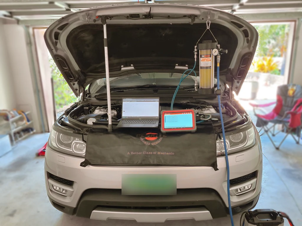 Diesel SUV in a garage with its bonnet open, connected cleaning equipment, a laptop and diagnostic tablet; number plate blurred
